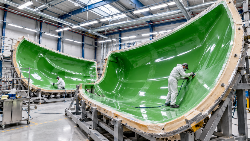 Workers applying surface coatings inside large composite molds in an industrial manufacturing facility.
