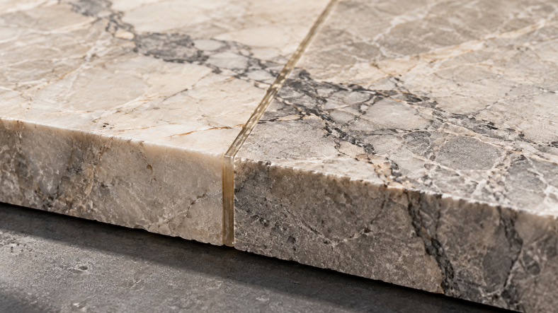 Close-up of two natural marble slabs joined with a transparent stone adhesive, showing a precise bonding seam along the stone edges.