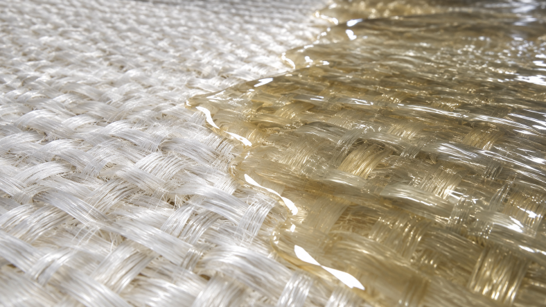 Close-up of liquid resin impregnating woven fiberglass fabric, illustrating resin flow and fiber wet-out in composite lamination.